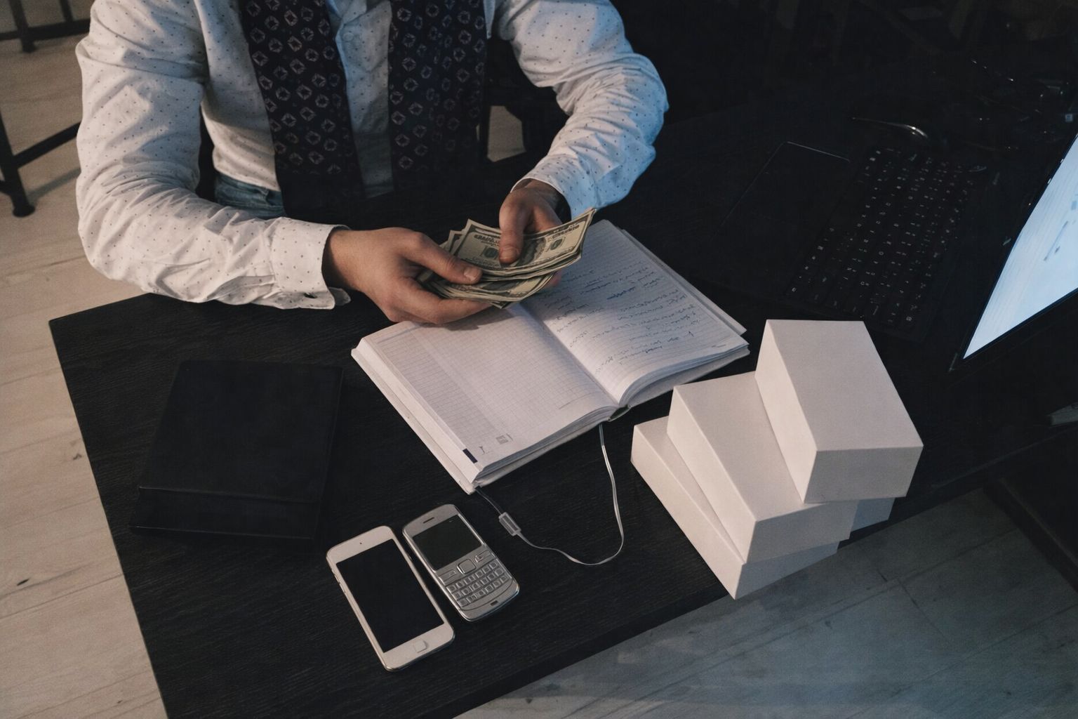 En person räknar sedlar vid ett skrivbord med dokument och mobiler.