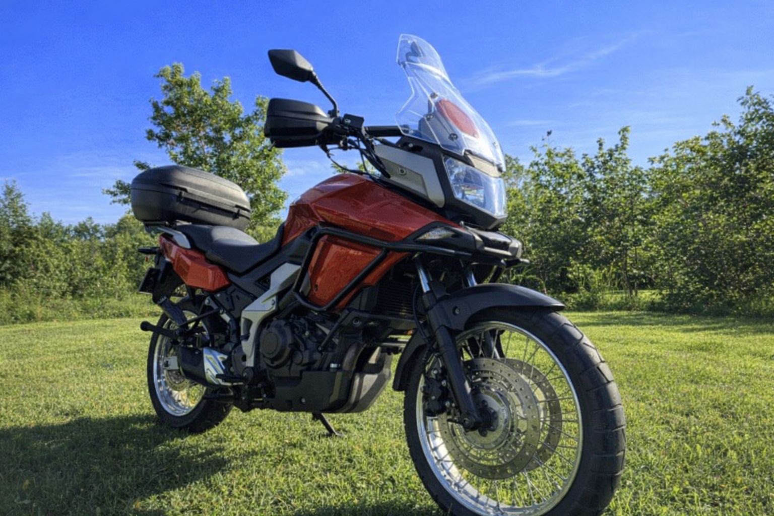 En röd och svart motorcykel av äventyrsmodell på en gräsmatta.