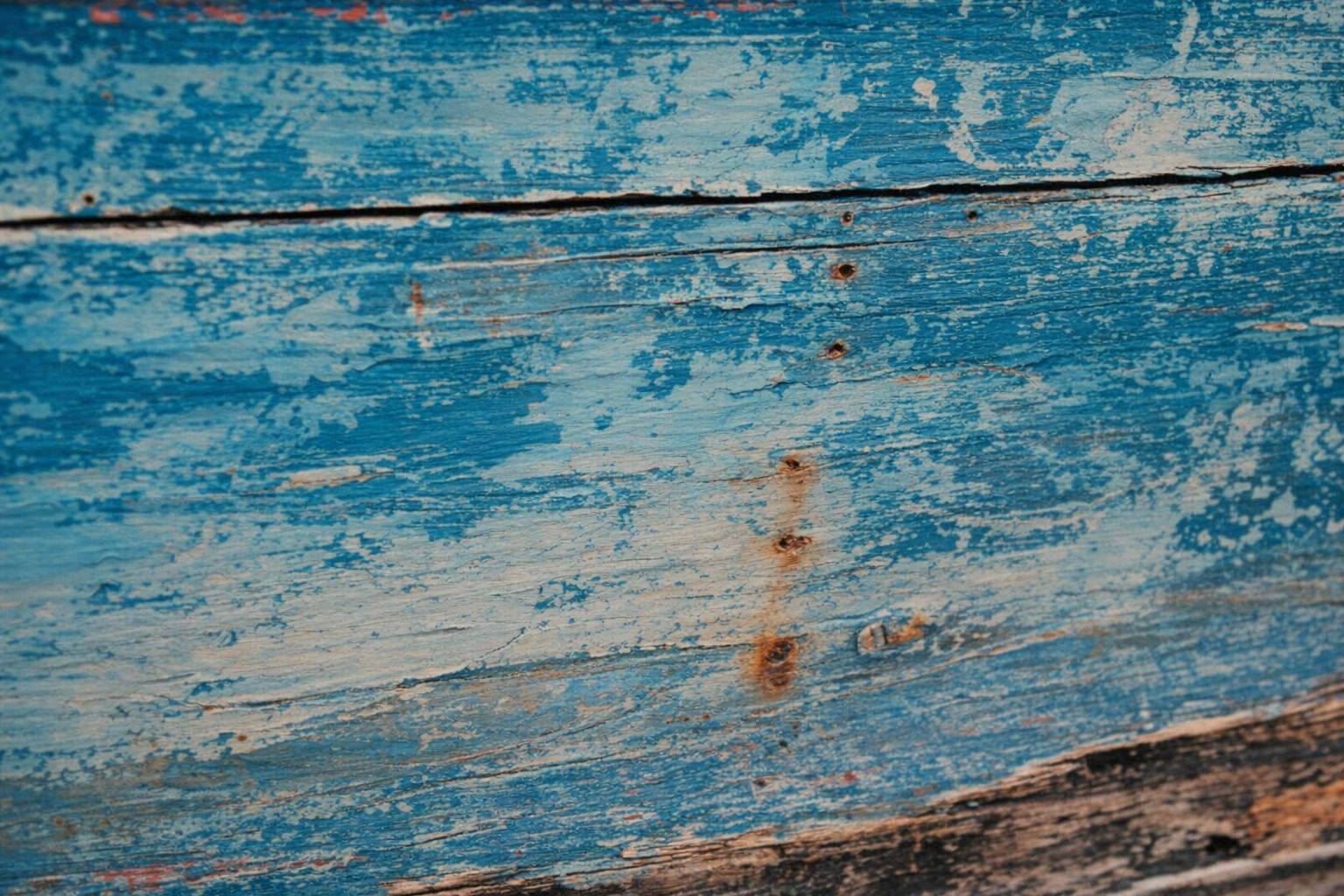 Närbild av sliten, flagnad blå målarfärg på ett äldre fordonschassi av trä.